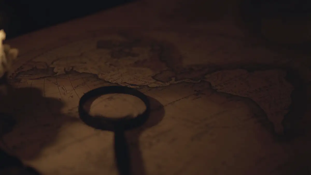 A candle, an old key-shaped magnifier and a map on a dark table