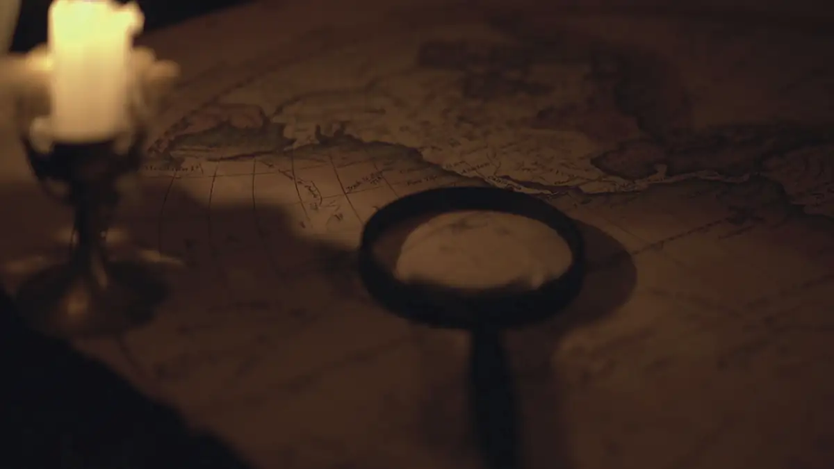 A candle, an old key-shaped magnifier and a map on a dark table