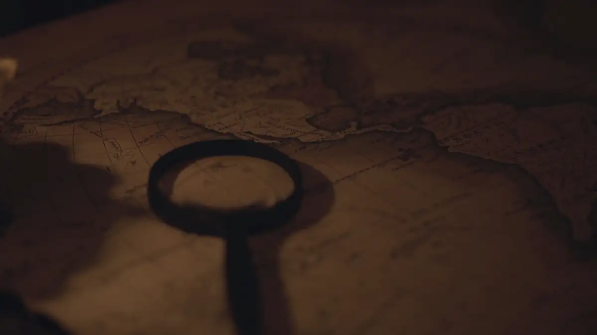 A candle, an old key-shaped magnifier and a map on a dark table