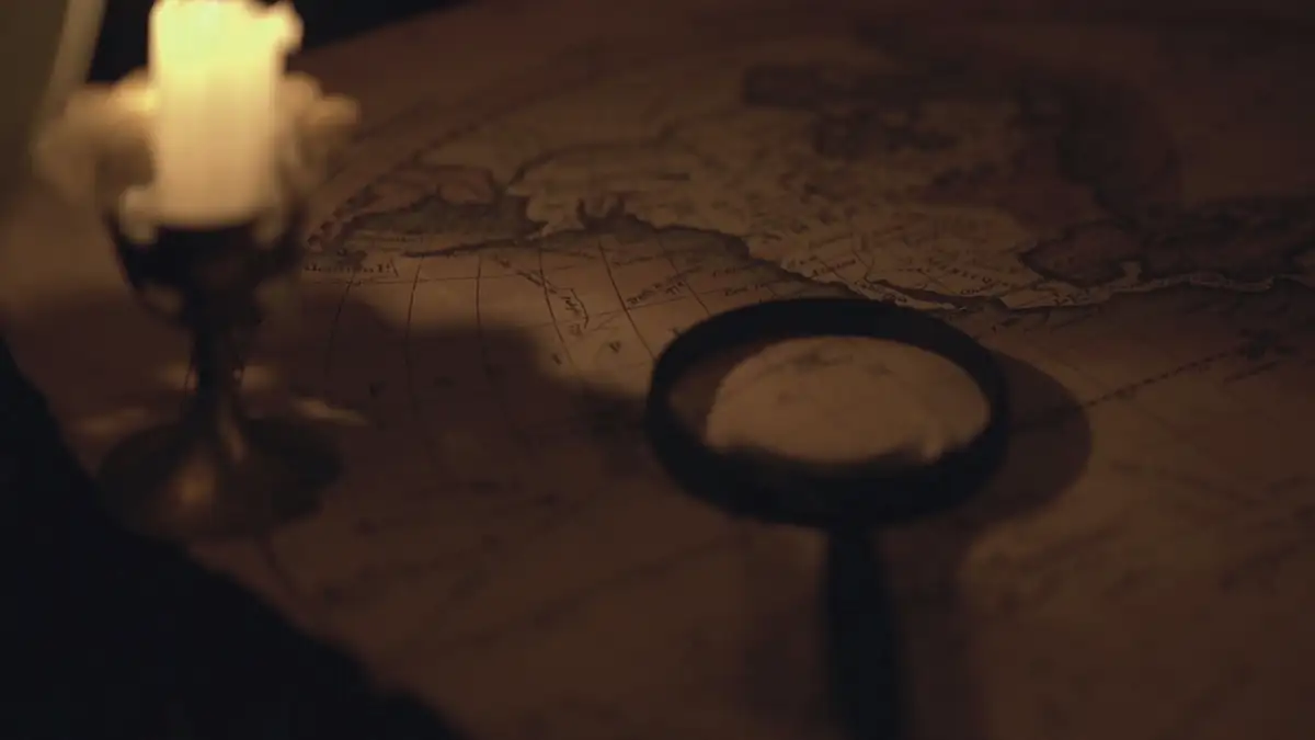 A candle, an old key-shaped magnifier and a map on a dark table